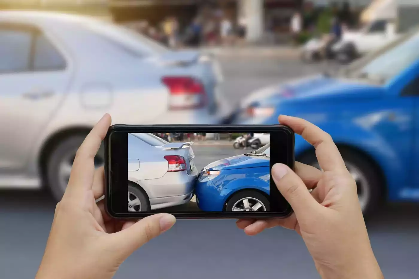 A person holding a phone to photograph a rear-end car accident scene.