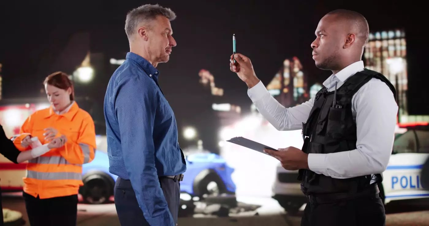 A police officer conducting a nighttime field sobriety test on a man using a pen tracker.