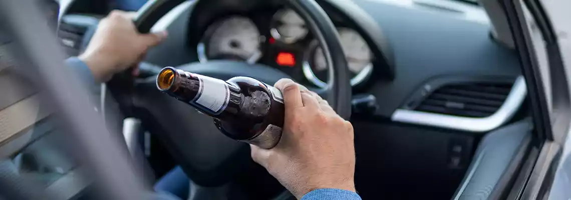 A person driving a car while holding an open bottle of beer in their hand.