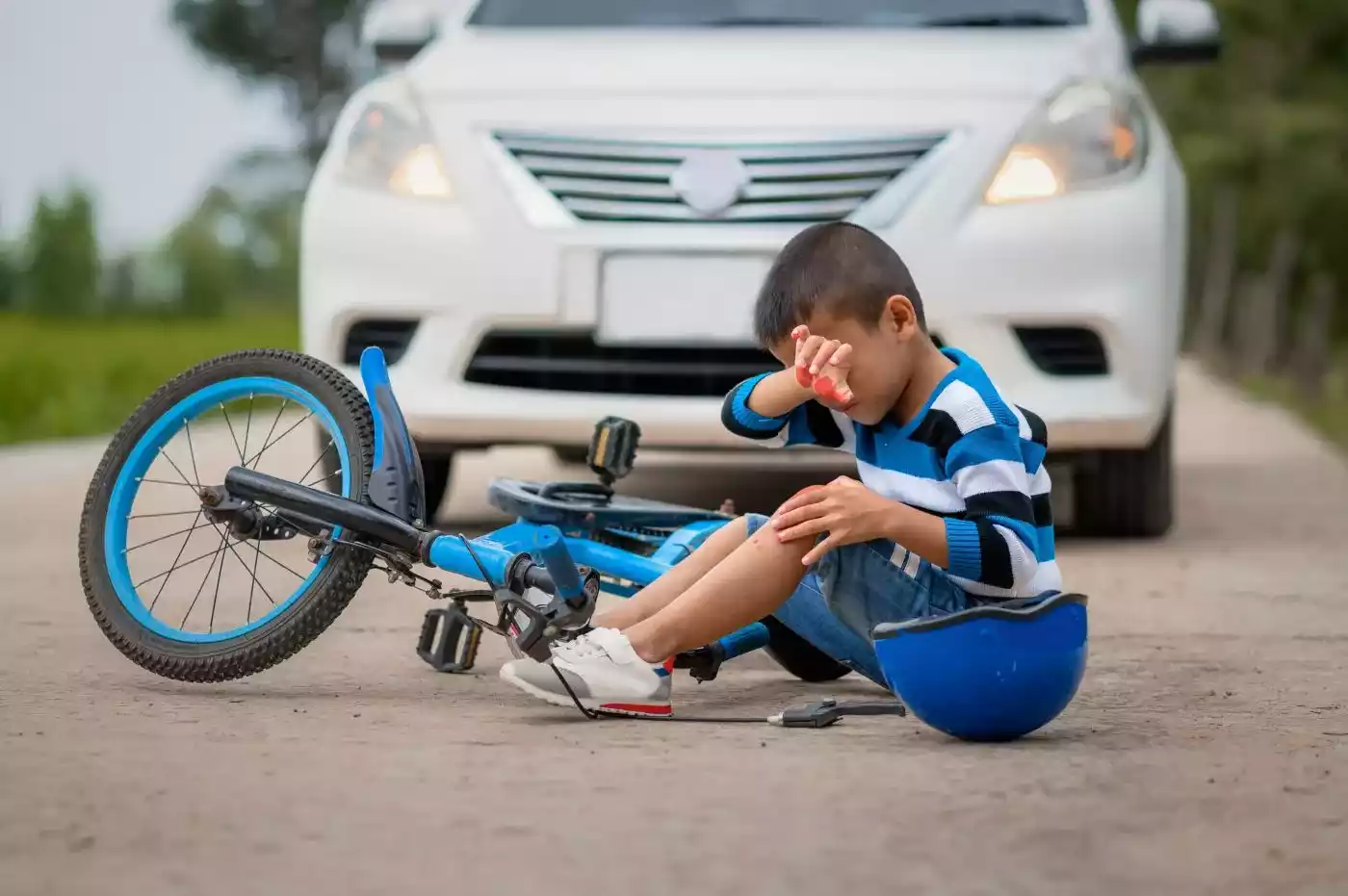 A crying boy was injured because his bicycle collided with a car on the road.
