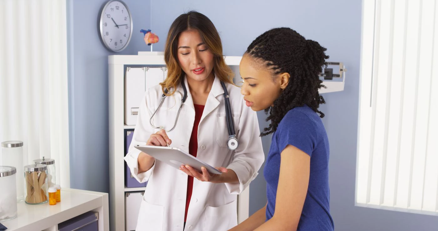 A female doctor in a white coat shows medical results on a tablet to a patient.