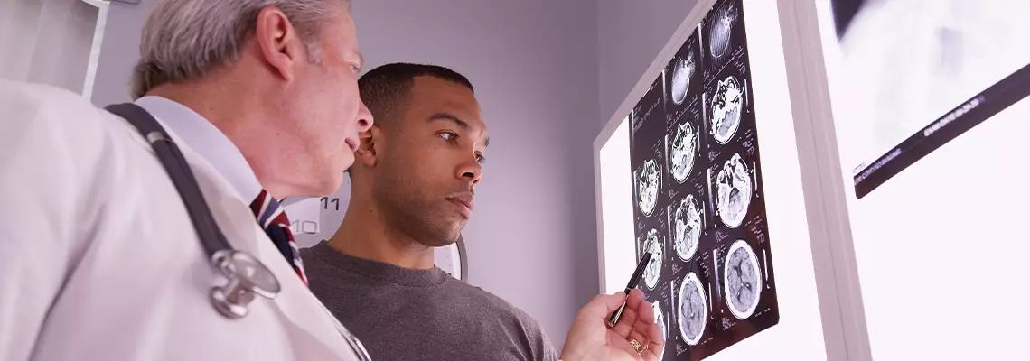 A medical doctor and a male patient examining head CT scans on a lightbox.