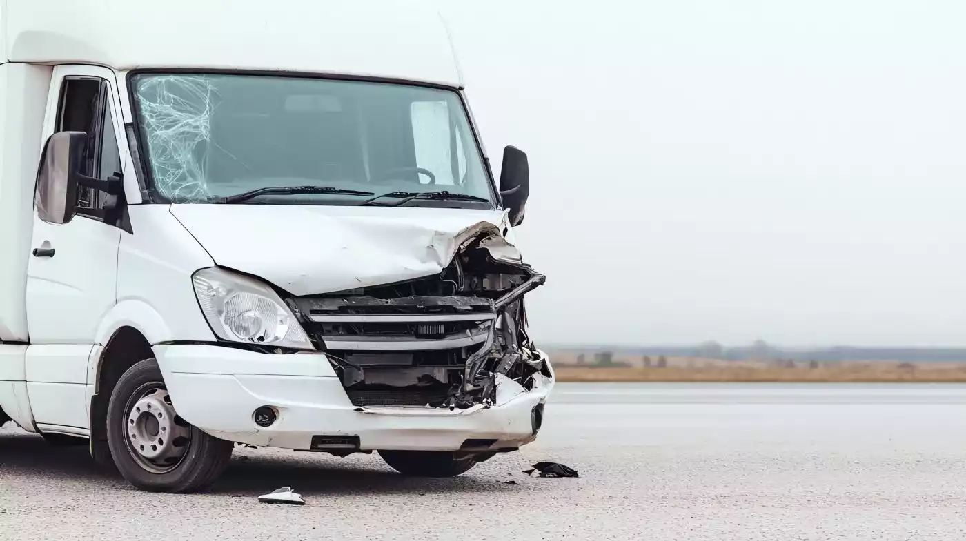 A white delivery van with severe front-end damage from a crash on a highway roadside.