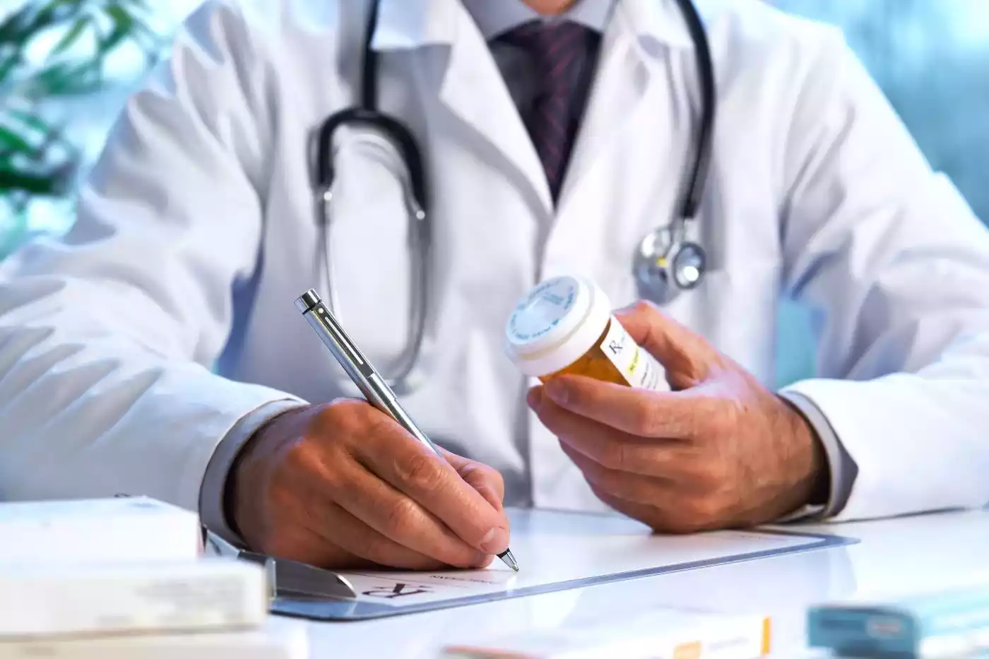 A close-up of a doctor writing on a clipboard while holding a prescription pill bottle.