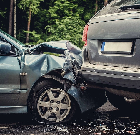 Two cars involved in a rear-end collision on a forest-lined road, with visible damage to the front of one car and rear of the other.