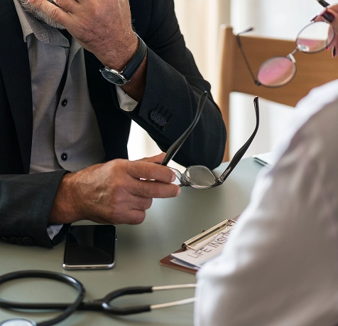 Two men, one in a suit and one in a white coat, seated at a table discussing a life insurance document, with eyeglasses and a stethoscope visible.