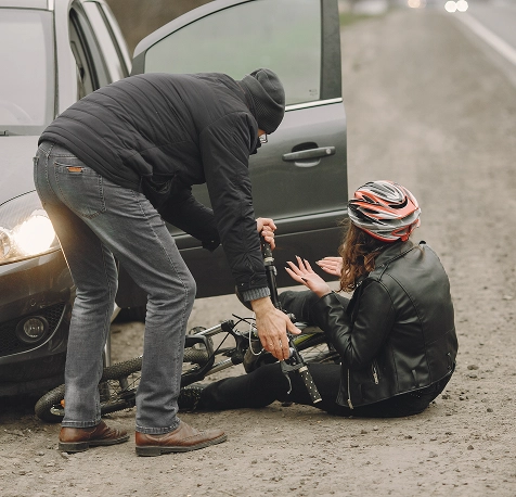 Man assists female cyclist who fell off her bike beside a car on a roadside.