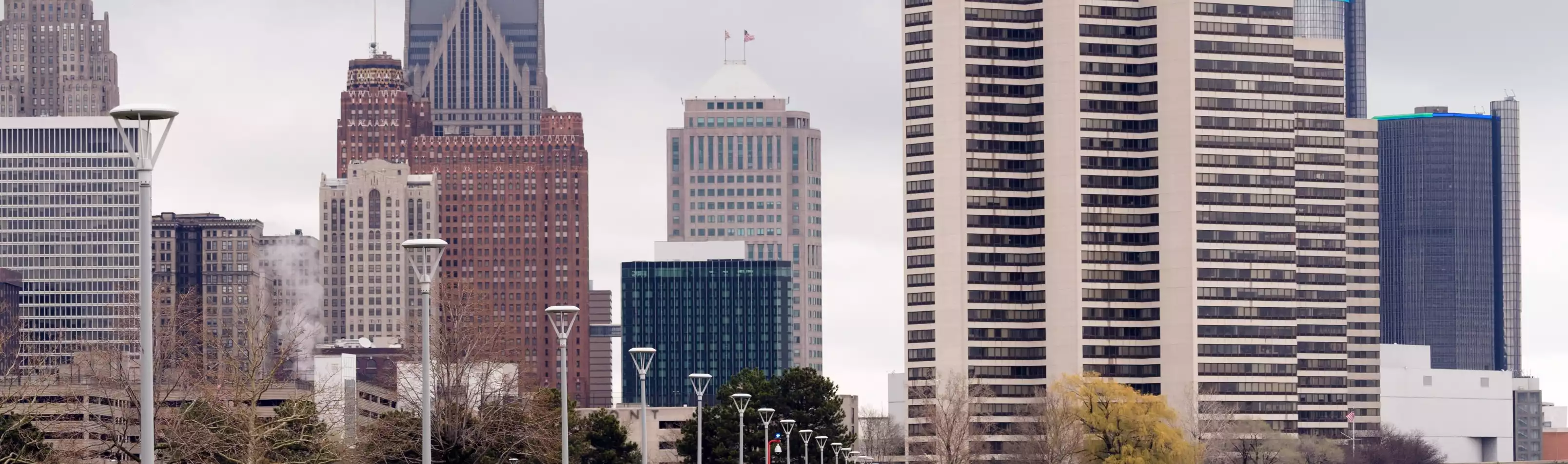 Detroit International Riverwalk path facing the city skyline and skyscrapers on a cloudy day.